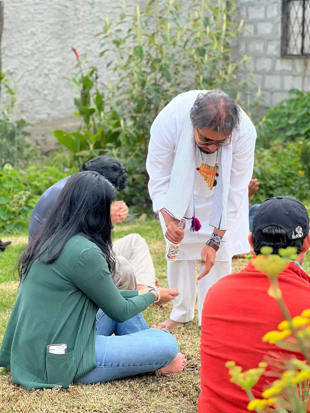 Spiritual leader blessing participants with sacred water during a ceremonial cacao gathering in an open garden space