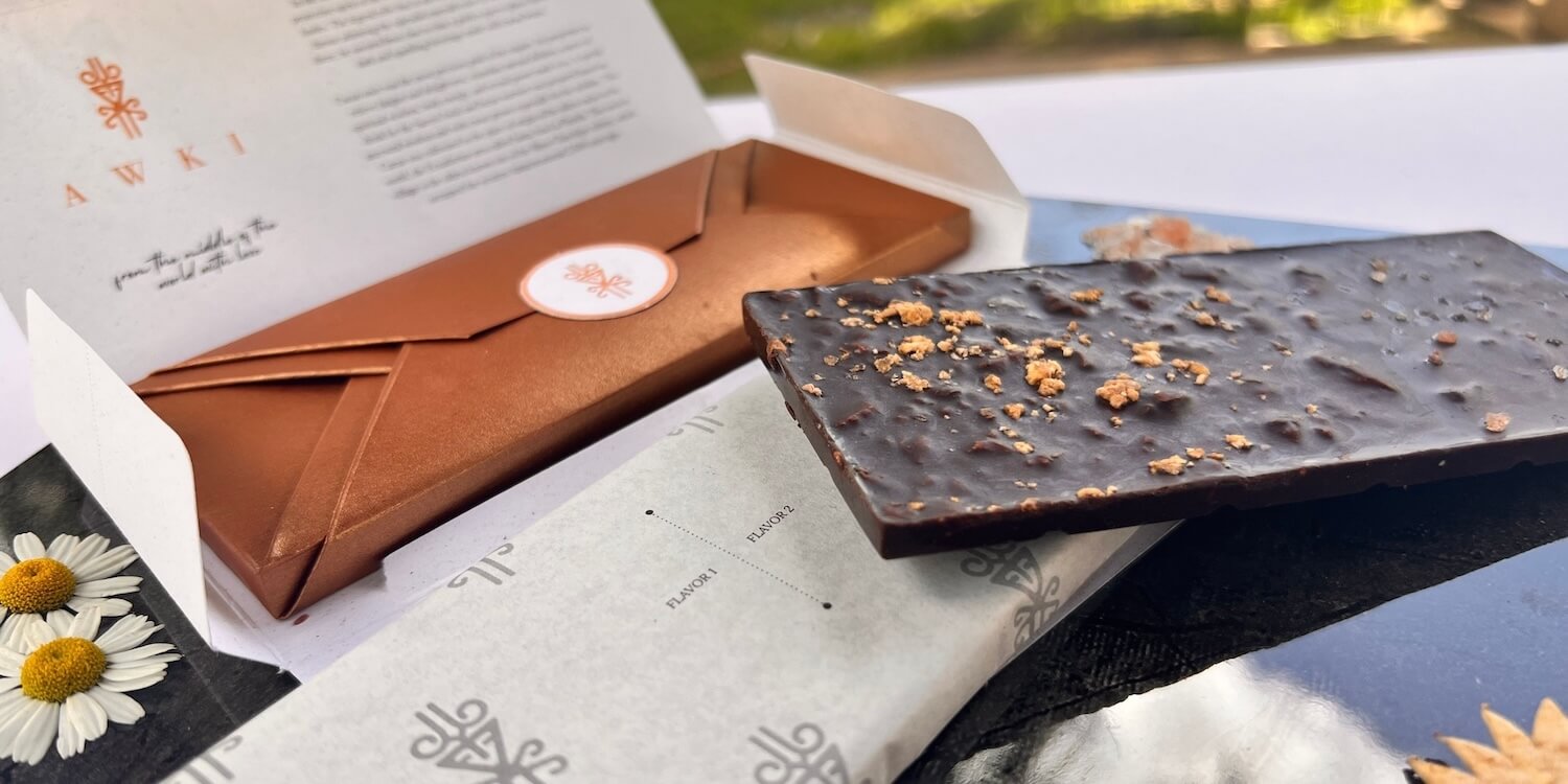 Cognitive Collection chocolate bar displayed with open copper envelope packaging and floral backdrop.