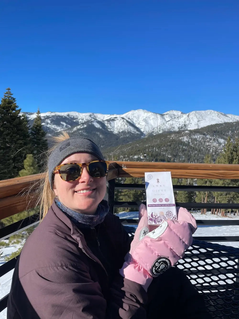 Woman holding Awki Divvy chocolate bar in snowy mountain setting with bright winter sunlight and scenic alpine views
