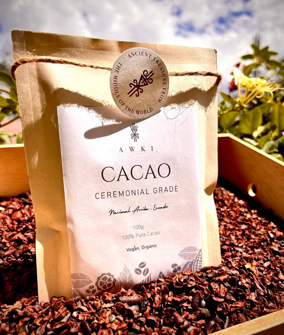 Close-up of Awki ceremonial cacao pouch on a bed of cacao nibs with sky and flowers in the background
