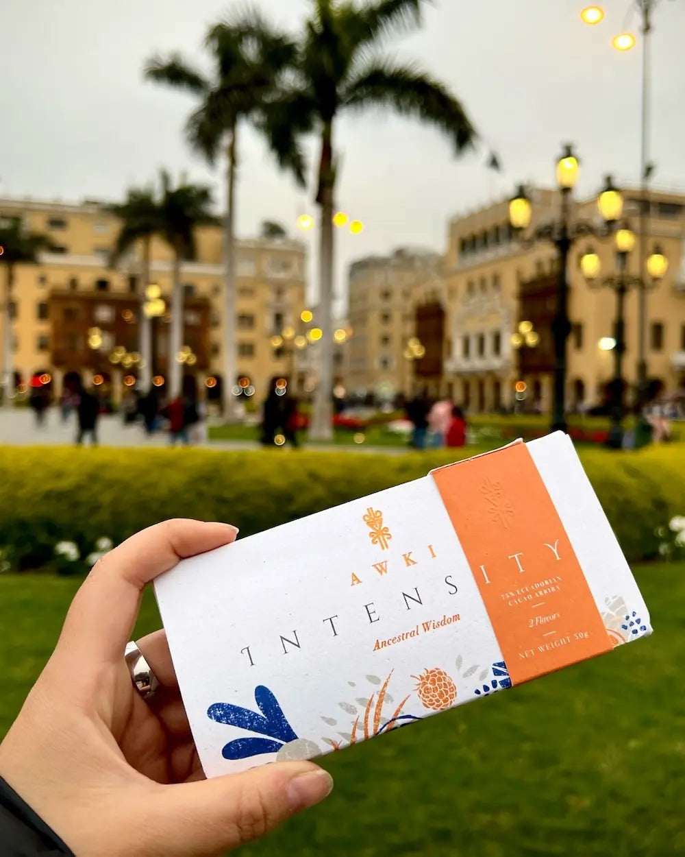 Awki Intensity chocolate bar held in front of a historic city square with palm trees and colonial architecture