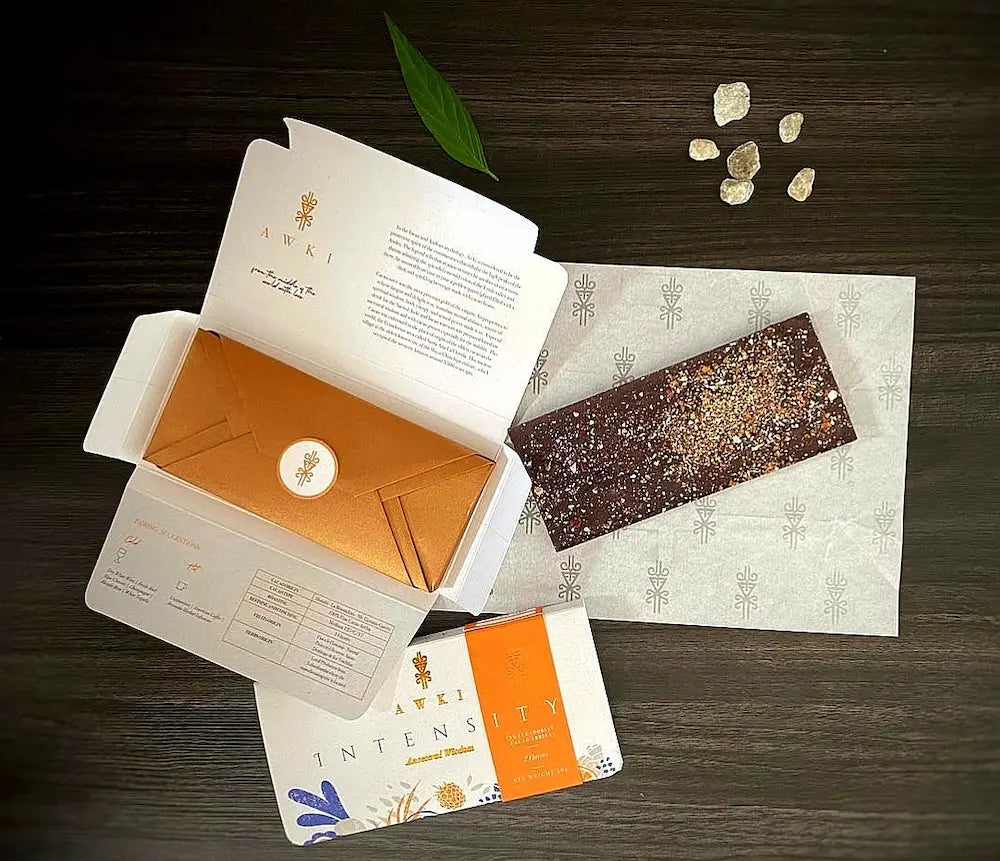 AWKI Intensity dark chocolate bar unwrapped with visible cacao nib toppings, next to luxury copper envelope packaging.