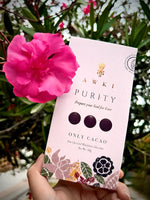 Awki Purity cacao bar 50g held next to a vibrant pink flower outdoors