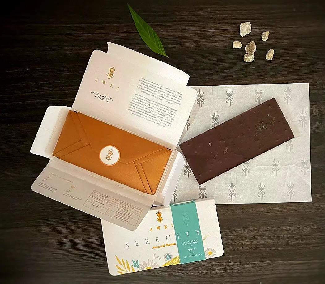 Awki SERENITY chocolate bar unwrapped next to open golden envelope and cacao beans