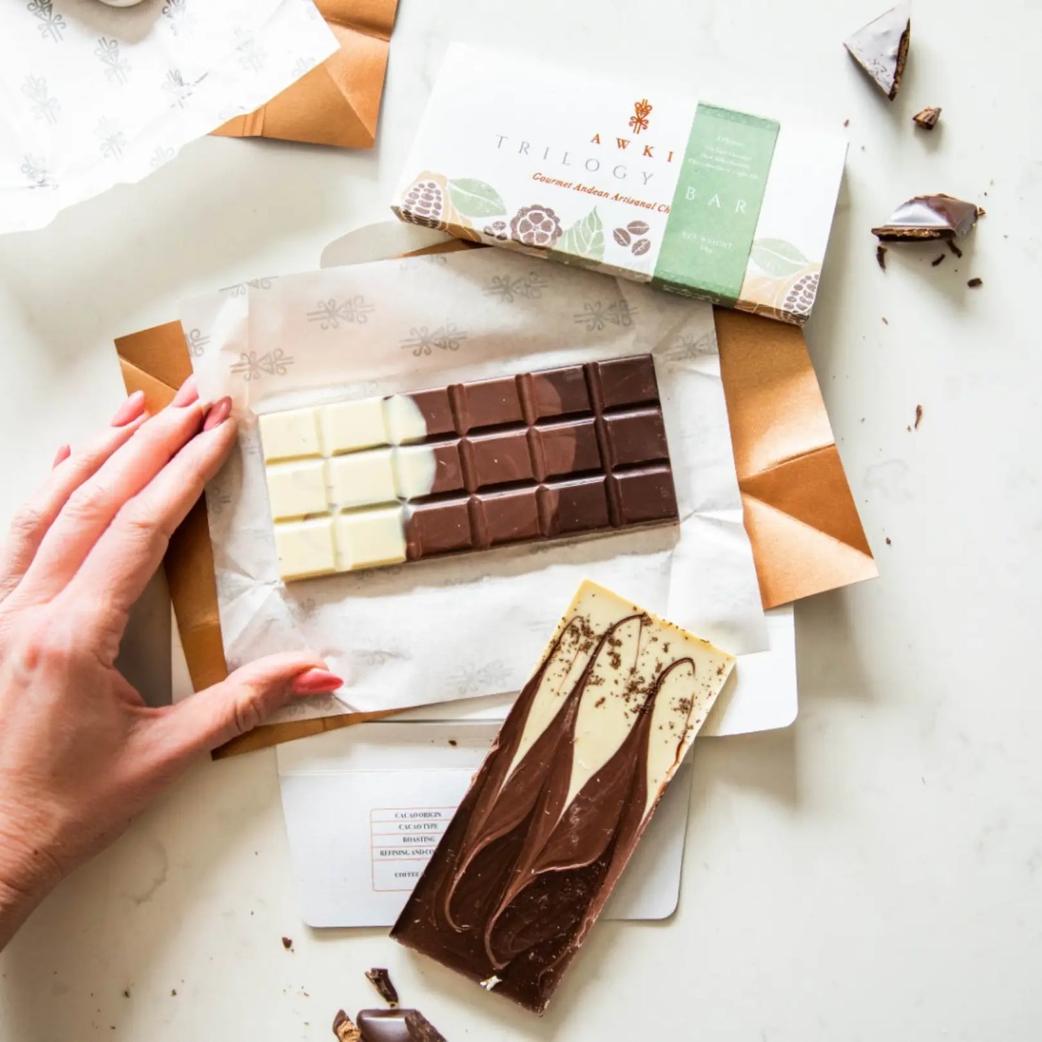 Awki Trilogy artisanal chocolate bar featuring three flavors—white, milk, and dark—unwrapped with elegant eco-packaging on a marble surface