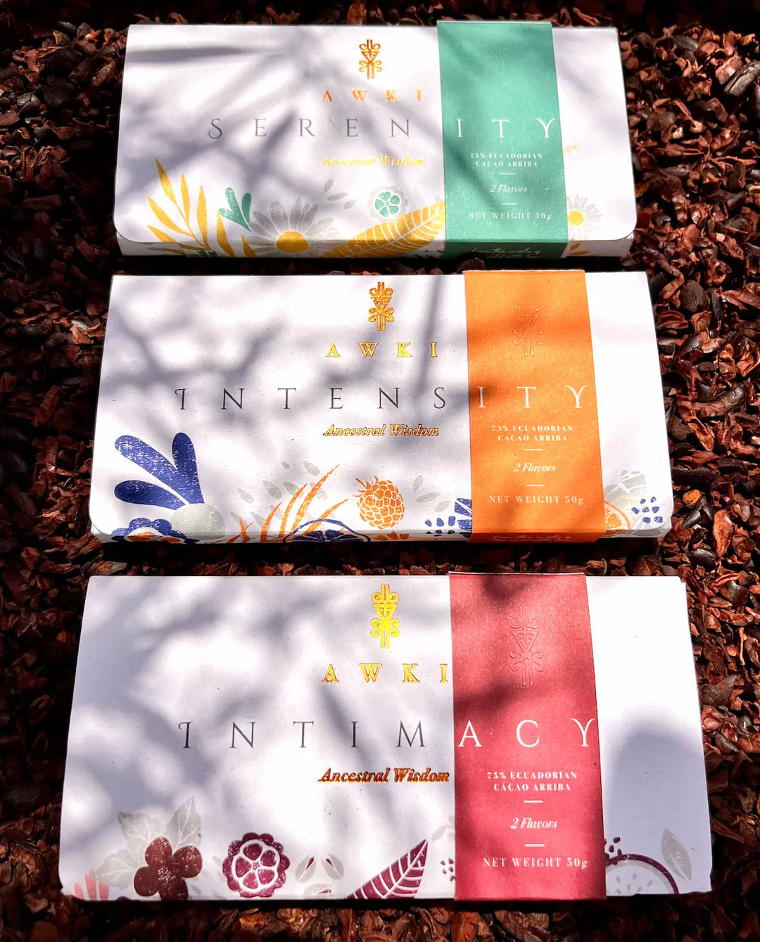 Awki Serenity, Intensity, and Intimacy chocolate bars displayed on a bed of cacao nibs with natural sunlight and shadow patterns