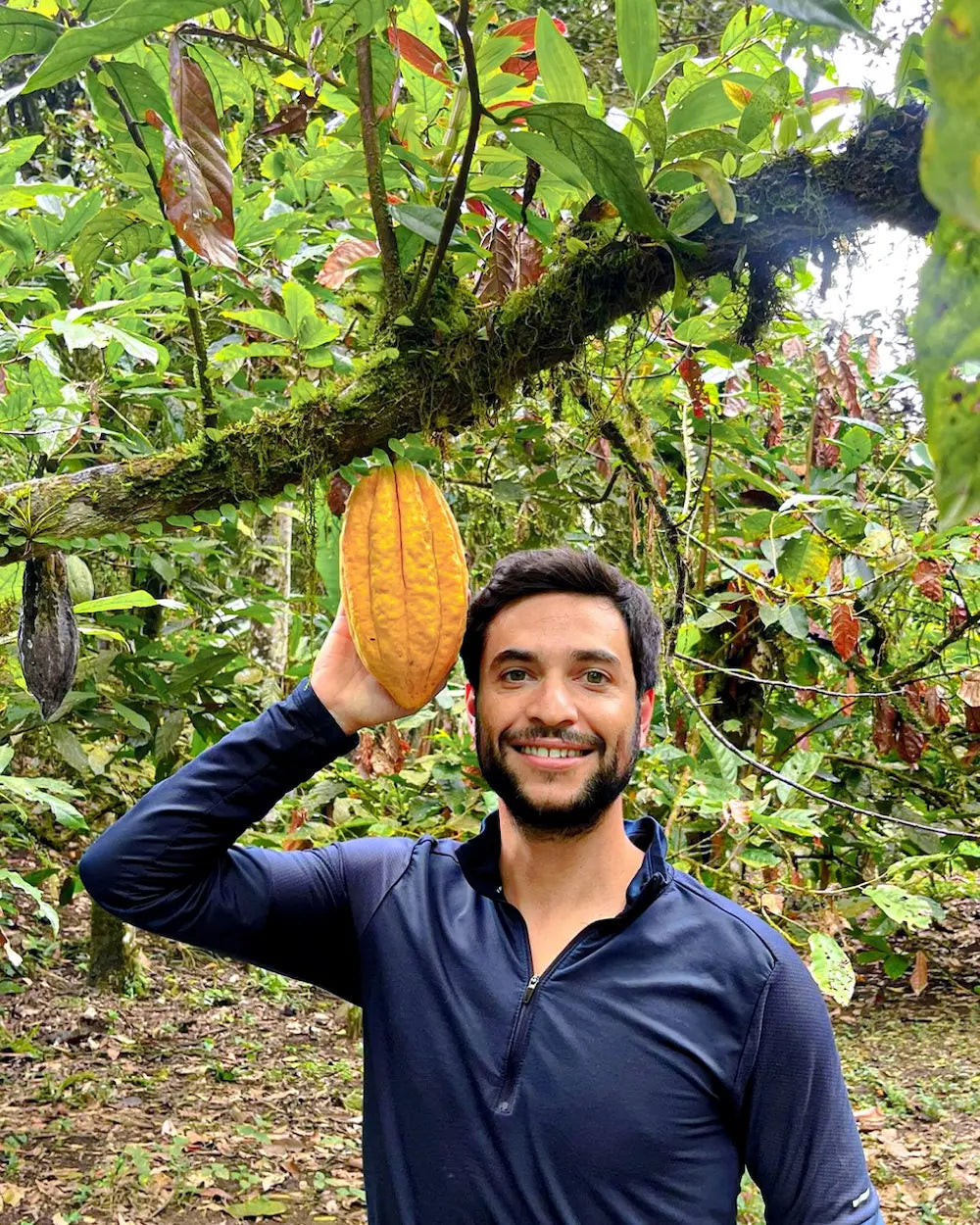 Founder of Awki USA smiling and holding a ripe cacao pod in an Ecuadorian cacao farm