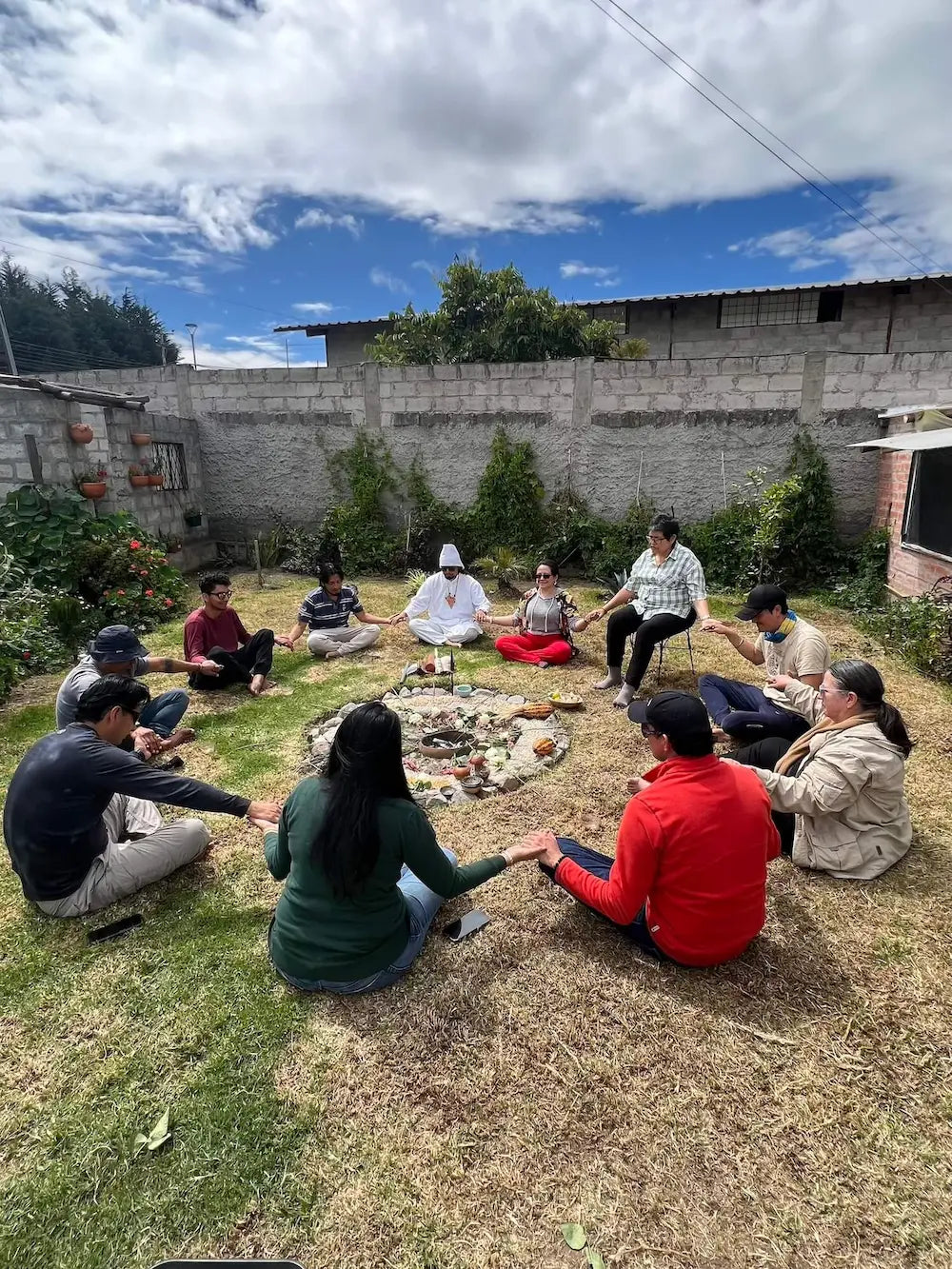Participants holding hands in a circle around a ceremonial cacao altar during a community ritual under the open sky